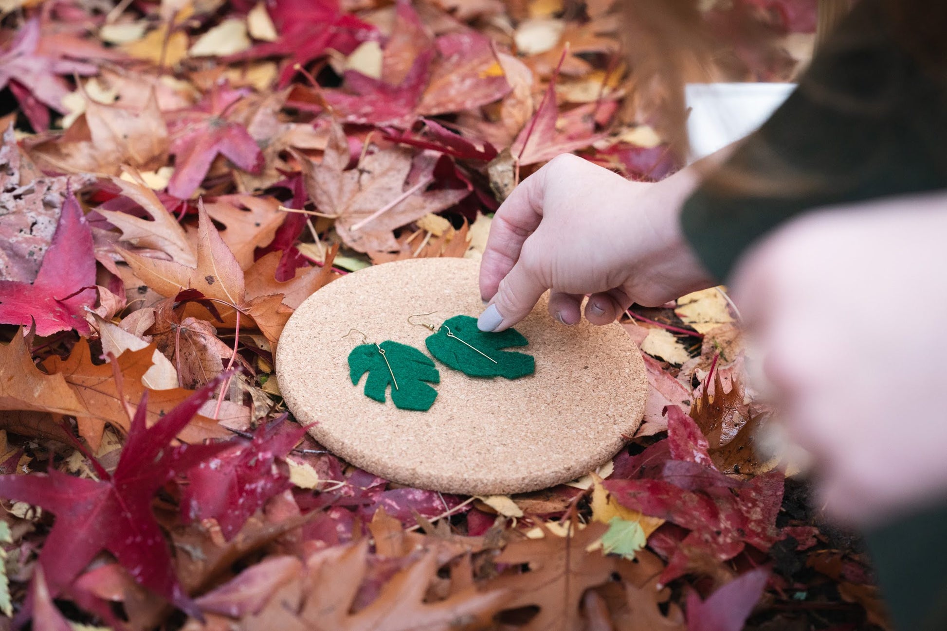 Model picking up a Jungle Monstera leaf felt earring from an autumn photo shoot