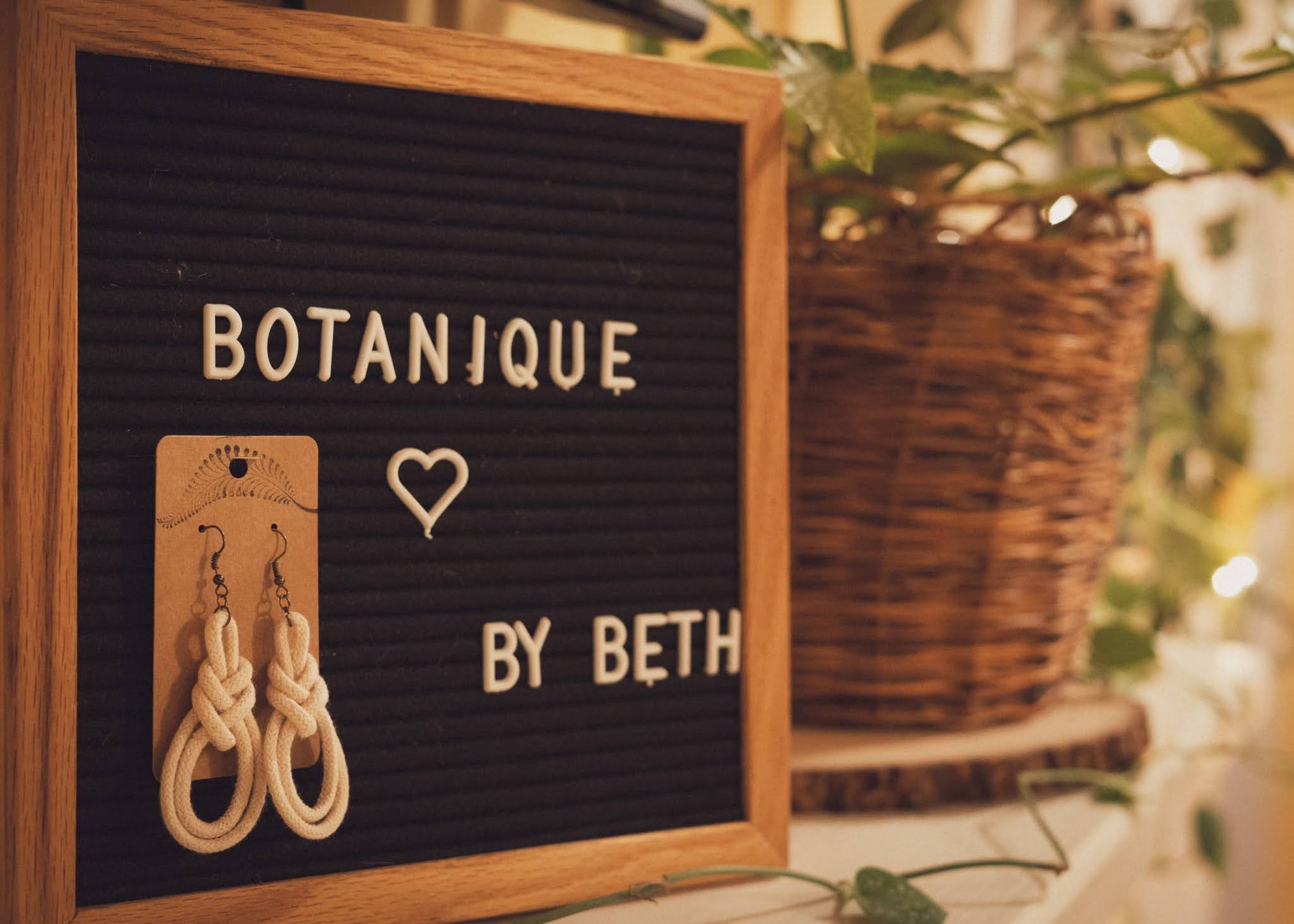 Double Macrame Loop earrings hanging on a Botanique sign with lovely houseplants in the background on a mantle