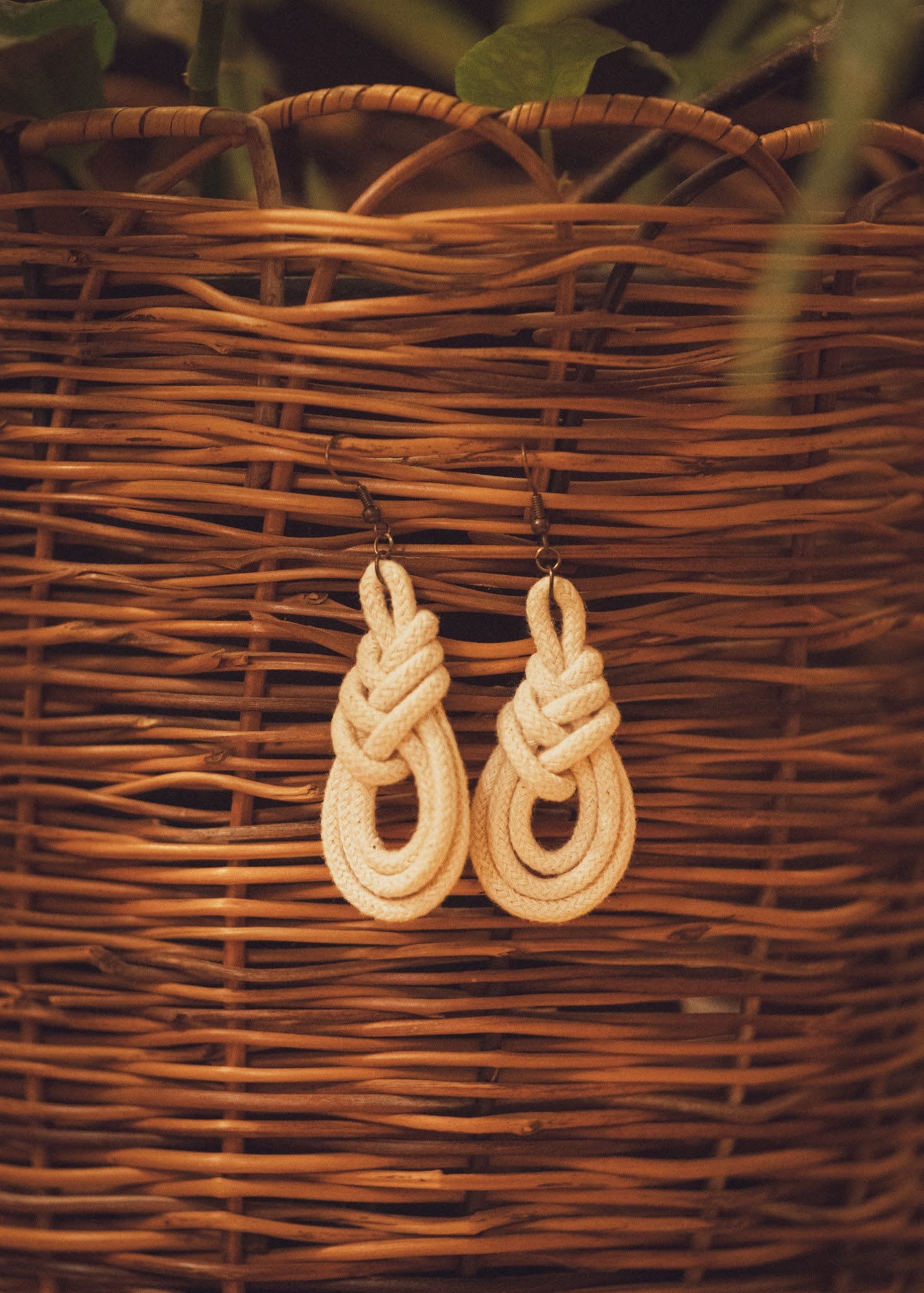 Triple Macrame Loop earrings hanging on a wicker basket with a houseplant in the background